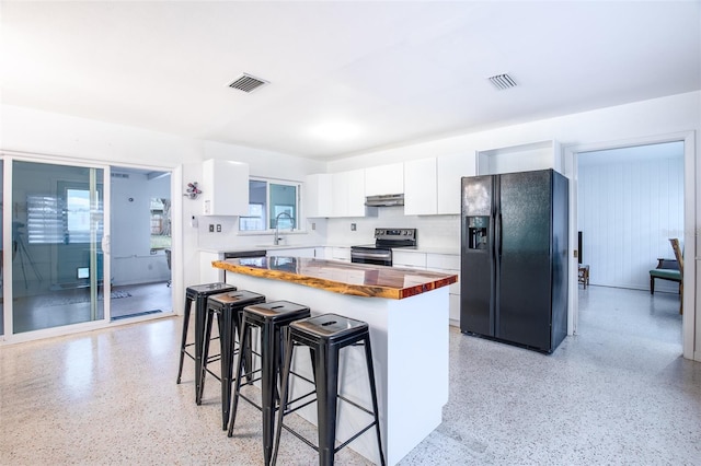 kitchen with a kitchen bar, white cabinetry, stainless steel range with electric stovetop, black fridge, and butcher block countertops