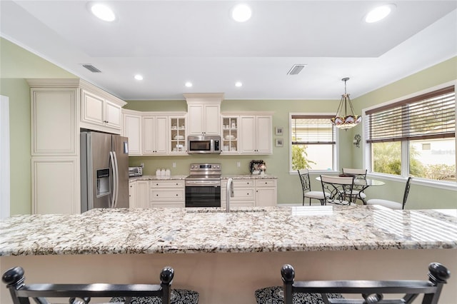 kitchen with sink, hanging light fixtures, a kitchen breakfast bar, stainless steel appliances, and light stone countertops