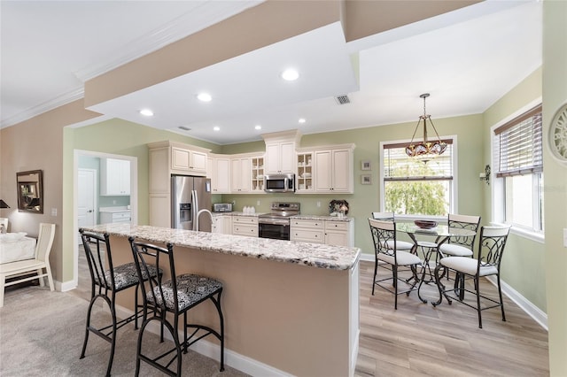 kitchen with a breakfast bar area, appliances with stainless steel finishes, hanging light fixtures, light stone counters, and ornamental molding