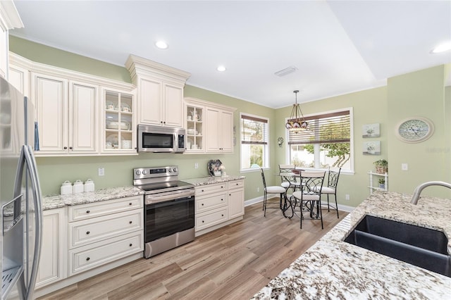 kitchen featuring decorative light fixtures, sink, light stone counters, stainless steel appliances, and light wood-type flooring