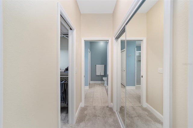 corridor featuring light colored carpet, baseboards, and light tile patterned floors