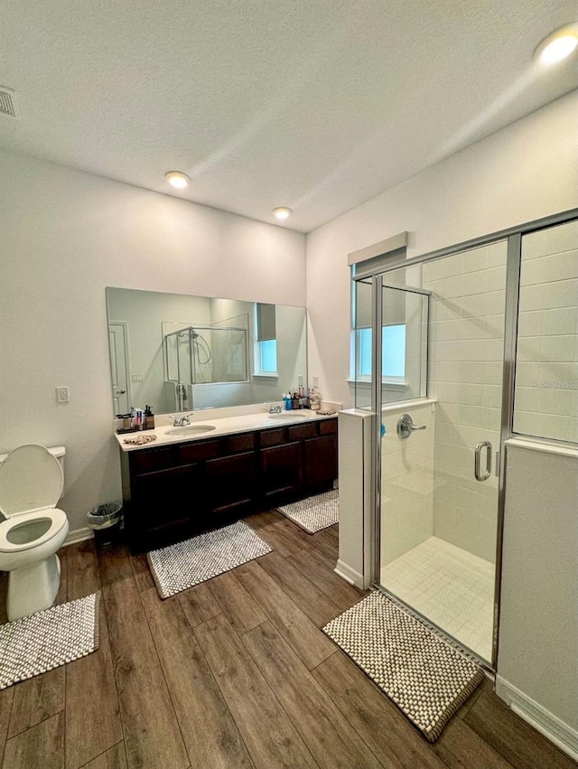 bathroom with wood-type flooring, toilet, a textured ceiling, walk in shower, and vanity