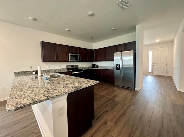 kitchen featuring light stone countertops, dark brown cabinetry, appliances with stainless steel finishes, sink, and kitchen peninsula