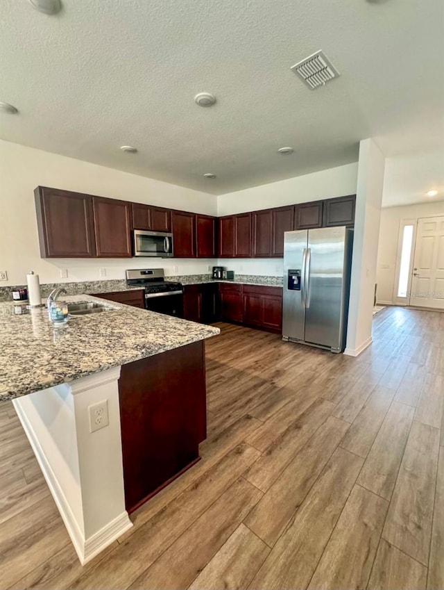 kitchen featuring light hardwood / wood-style floors, light stone countertops, sink, kitchen peninsula, and stainless steel appliances