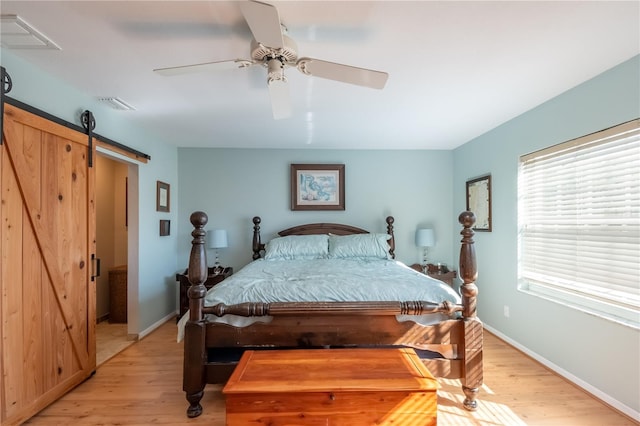 bedroom with a barn door, ceiling fan, and light wood-type flooring