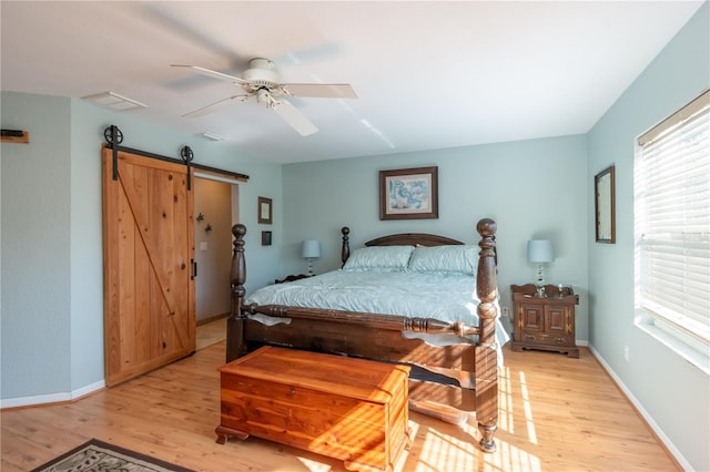 bedroom with ceiling fan, a barn door, and light wood-type flooring