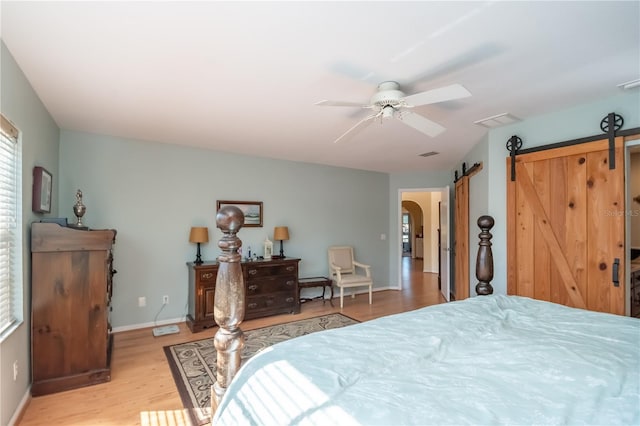 bedroom with ceiling fan, a barn door, and light hardwood / wood-style floors