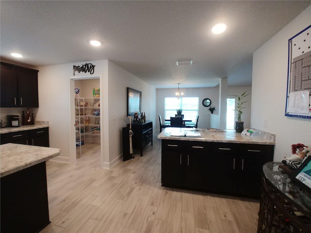 kitchen with hanging light fixtures, light hardwood / wood-style floors, a notable chandelier, and light stone countertops