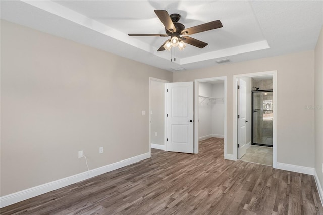 unfurnished bedroom featuring ceiling fan, a raised ceiling, a closet, and ensuite bath