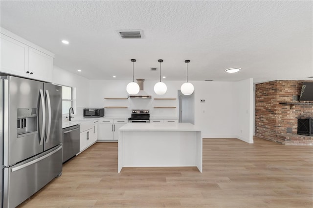 kitchen with decorative light fixtures, light wood-type flooring, appliances with stainless steel finishes, a fireplace, and white cabinets