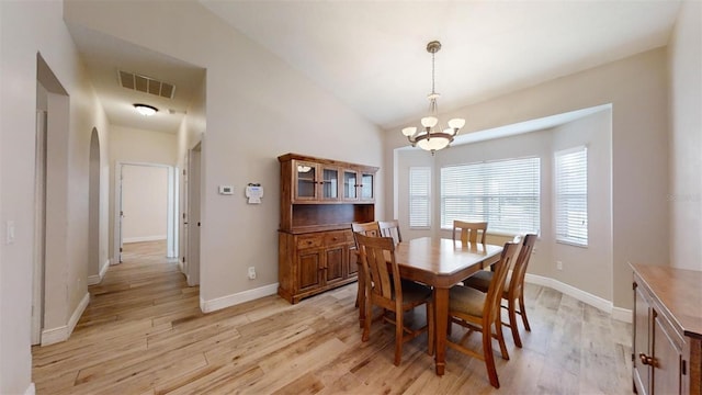 dining area with light wood-type flooring, a chandelier, and vaulted ceiling