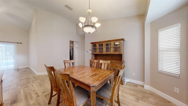 dining room with light hardwood / wood-style floors, vaulted ceiling, and an inviting chandelier