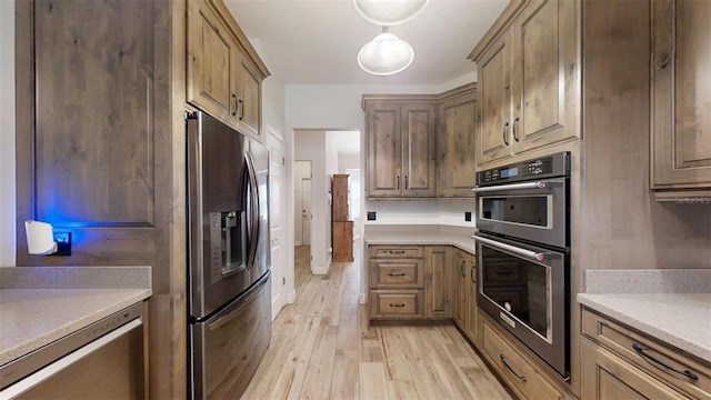 kitchen featuring light wood-type flooring, stainless steel appliances, and pendant lighting