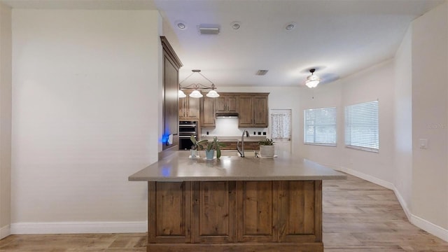 kitchen with ceiling fan, hanging light fixtures, sink, light hardwood / wood-style floors, and stainless steel double oven