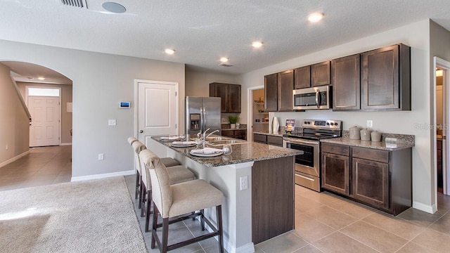 kitchen with light tile patterned floors, sink, an island with sink, stainless steel appliances, and a breakfast bar area