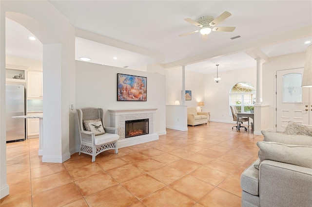 tiled living room with a tiled fireplace, ceiling fan, and ornate columns