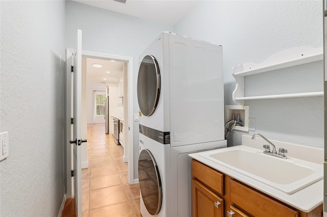 clothes washing area featuring light tile patterned floors, sink, and stacked washer and clothes dryer