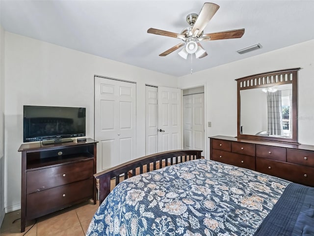 bedroom featuring tile patterned flooring, visible vents, two closets, and ceiling fan