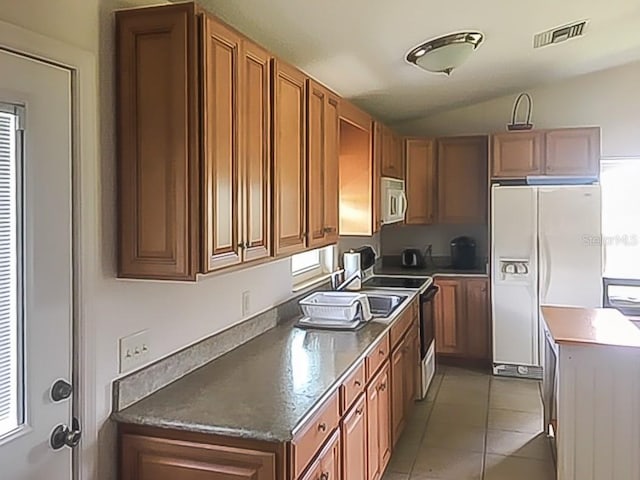 kitchen with light tile patterned floors, dark countertops, visible vents, white fridge with ice dispenser, and stainless steel microwave