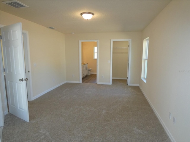 unfurnished bedroom featuring a walk in closet, connected bathroom, a closet, and light carpet