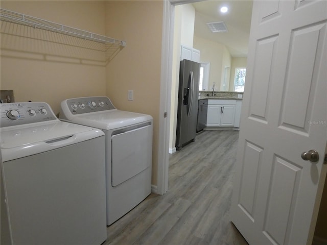 washroom with washing machine and dryer, sink, and light hardwood / wood-style floors