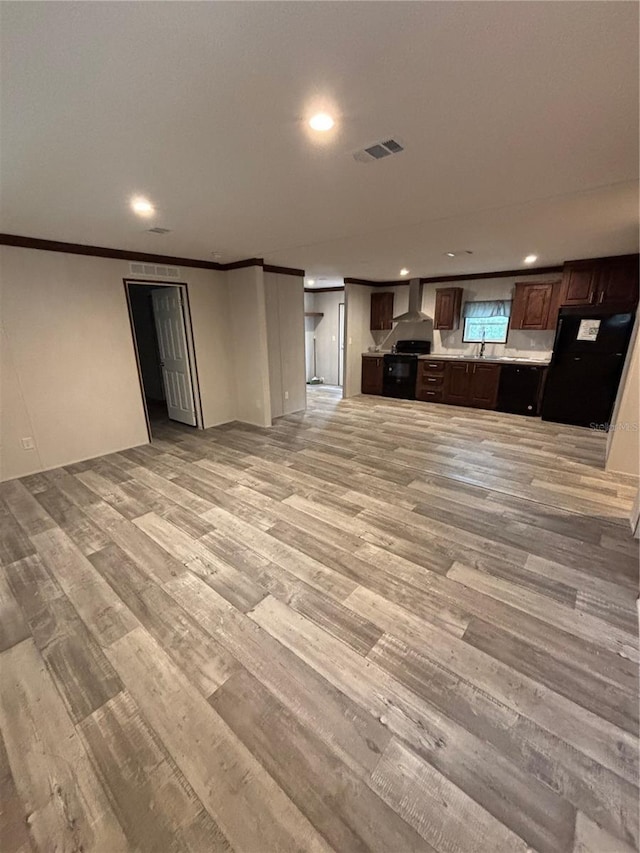 kitchen featuring wall chimney exhaust hood, sink, ornamental molding, light hardwood / wood-style flooring, and dark brown cabinets