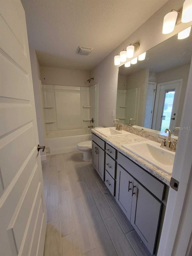 full bathroom featuring toilet, a textured ceiling, bathtub / shower combination, and vanity