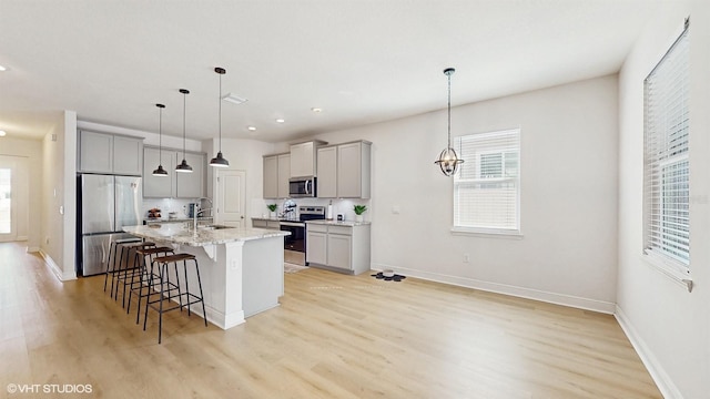 kitchen with a kitchen bar, sink, gray cabinetry, a center island with sink, and stainless steel appliances