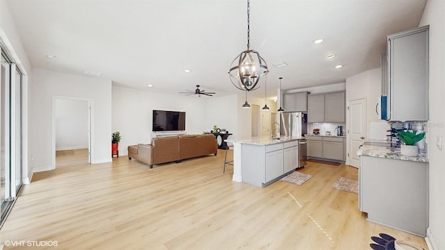 kitchen with decorative light fixtures, backsplash, a kitchen breakfast bar, a center island with sink, and light wood-type flooring