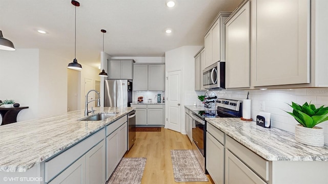 kitchen featuring appliances with stainless steel finishes, sink, gray cabinetry, hanging light fixtures, and light wood-type flooring