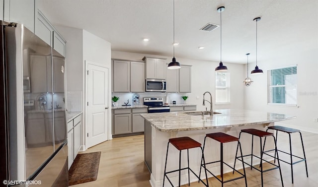 kitchen with decorative light fixtures, sink, gray cabinetry, a kitchen island with sink, and stainless steel appliances