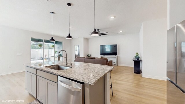 kitchen with light stone counters, hanging light fixtures, sink, and a center island with sink