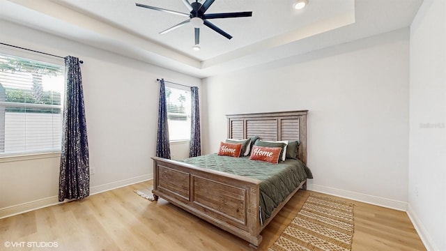 bedroom with ceiling fan, a raised ceiling, light hardwood / wood-style floors, and multiple windows