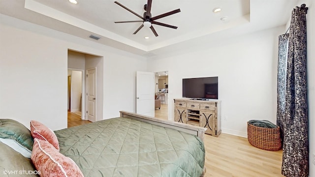 bedroom featuring hardwood / wood-style floors, a raised ceiling, and ceiling fan