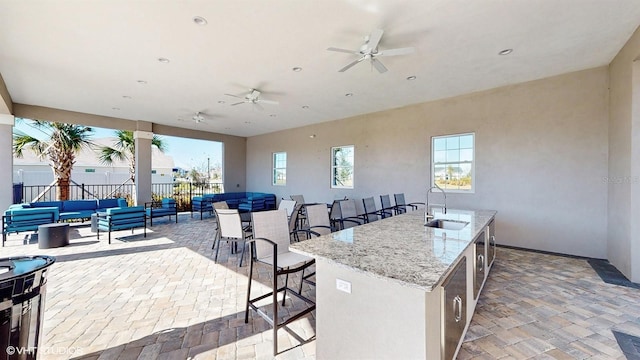 kitchen with sink, a breakfast bar area, light stone counters, a center island with sink, and ceiling fan