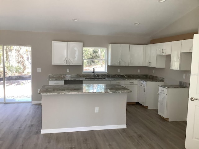 kitchen featuring stone counters, white cabinets, a center island, and a sink