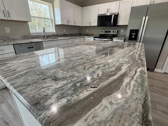 kitchen featuring light stone countertops, appliances with stainless steel finishes, light wood-style floors, white cabinetry, and a sink