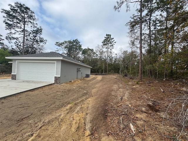 view of side of property with concrete driveway, central AC, stucco siding, a garage, and stone siding