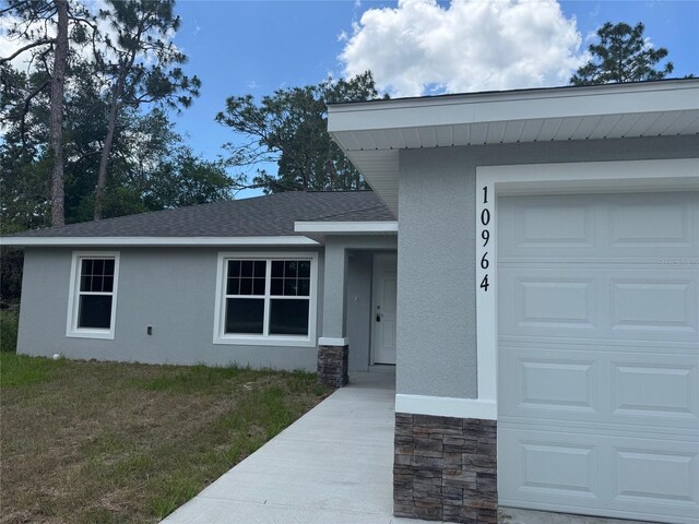 10964 N Frantz Ave, Citrus Springs, FL 34434 - view of exterior entry with stucco siding, stone siding, a shingled roof, a garage, and a lawn