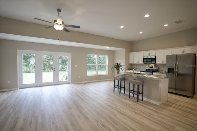 kitchen featuring white cabinets, light stone counters, a center island with sink, light hardwood / wood-style floors, and stainless steel appliances