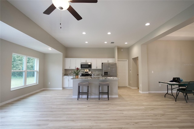 kitchen featuring a kitchen bar, light hardwood / wood-style floors, appliances with stainless steel finishes, white cabinetry, and a center island with sink