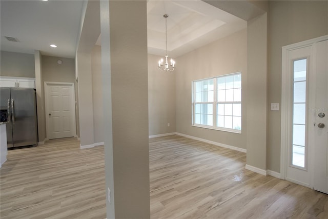 interior space with light hardwood / wood-style flooring, a notable chandelier, and a tray ceiling