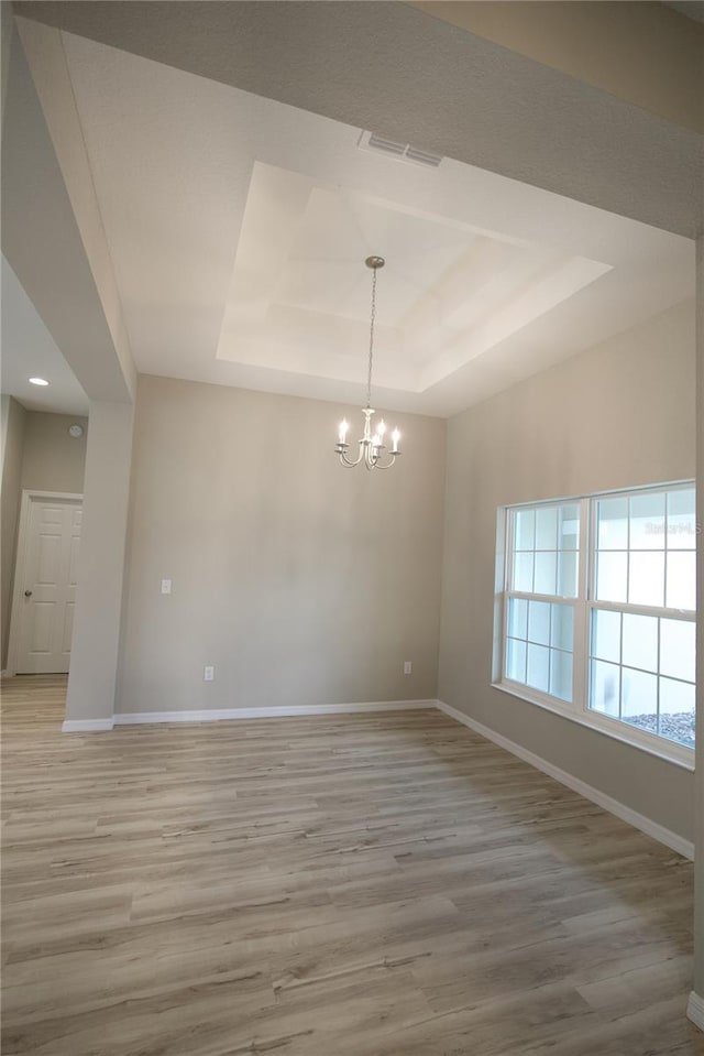 spare room with light hardwood / wood-style floors, a raised ceiling, and a chandelier