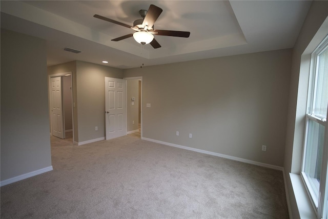 unfurnished room with ceiling fan, light colored carpet, and a raised ceiling