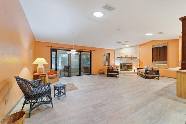 living room with light wood-type flooring, ceiling fan, a stone fireplace, and lofted ceiling