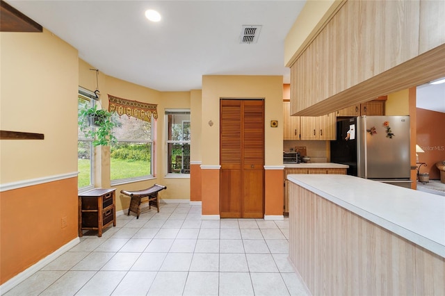 kitchen with light tile patterned flooring, light brown cabinetry, and stainless steel fridge