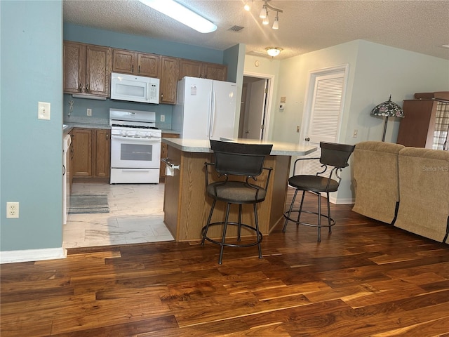 kitchen with a breakfast bar, a center island, white appliances, dark wood-type flooring, and a textured ceiling