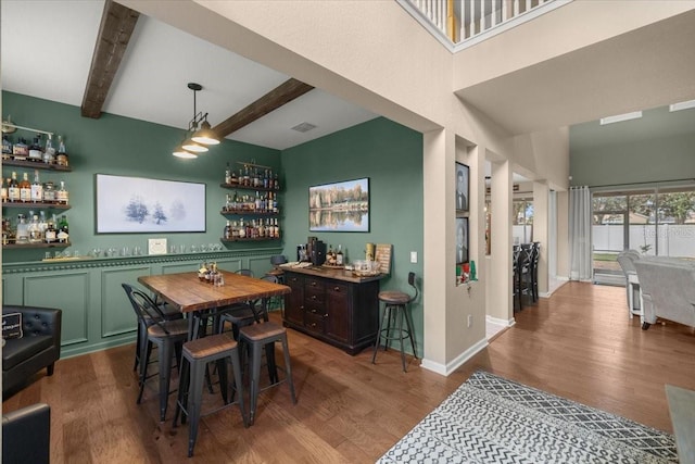 dining space featuring hardwood / wood-style floors, bar, and beamed ceiling