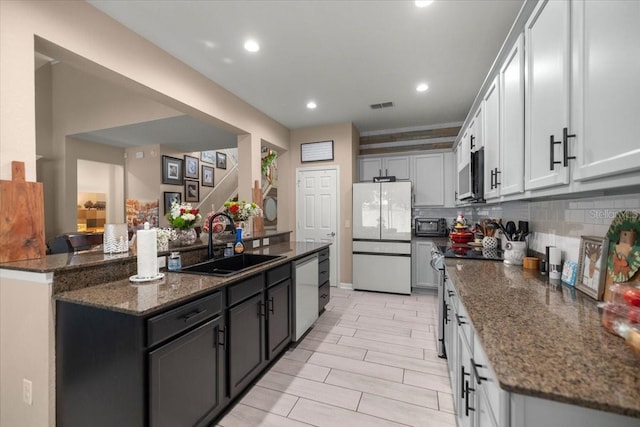 kitchen with sink, backsplash, white cabinets, dark stone countertops, and stainless steel appliances