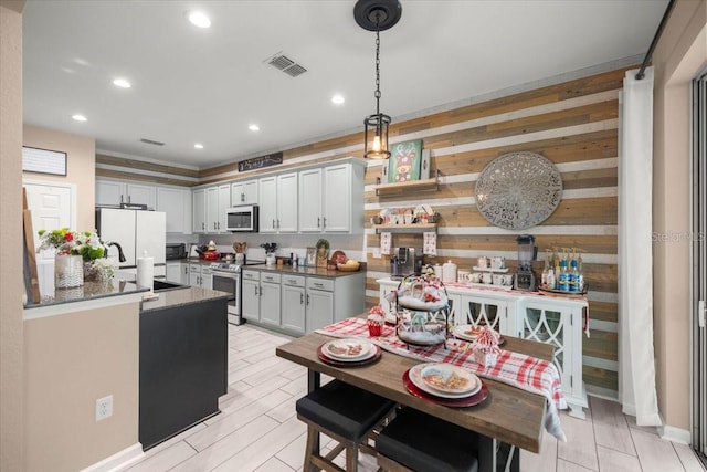 kitchen featuring wooden walls, sink, a kitchen island, decorative light fixtures, and stainless steel appliances